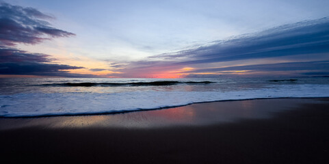 Blurred Background of Serene Sunset Over Calm Ocean Wave at Coastal Beach with Gentle Footprints in Soft Sand Landscape. Blurry Background For Design Projects.