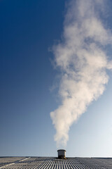 white smoke coming from a pipe against a blue sky background, white steam coming from a pipe during heating of a large industrial premises in cold weather