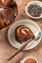 A piece of chocolate marble bundt cake or zebra cake with chocolate glaze on ceramic plate, brown table background, close up