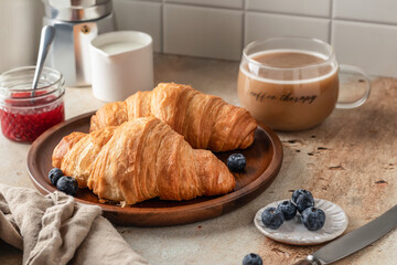 Delicious breakfast with croissants on wooden tray and coffee on white kitchen table background