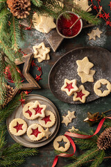 Homemade Linzer Christmas cookies filled with raspberry jam and dusted with sugar on ceramic plate with fir tree branches on wooden table top view