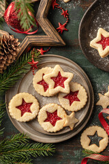 Homemade Linzer Christmas cookies filled with raspberry jam and dusted with sugar on ceramic plate with fir tree branches on wooden table top view