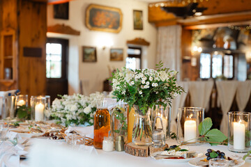 Elegant wedding banquet table with floral centerpiece, candles and drinks in a rustic interior prepared for festive reception indoors