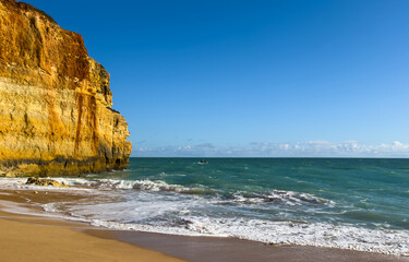 Beautiful sandy beach with red rocks and cliffs. Sunset at dusk with shallow waves on the Atlantic coast in Praia do Poco Velho, Praia da Falesia, Algarve, Portugal