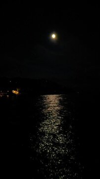 Aerial drone view of moon and moonlight reflected on sea waves at night, vertical background