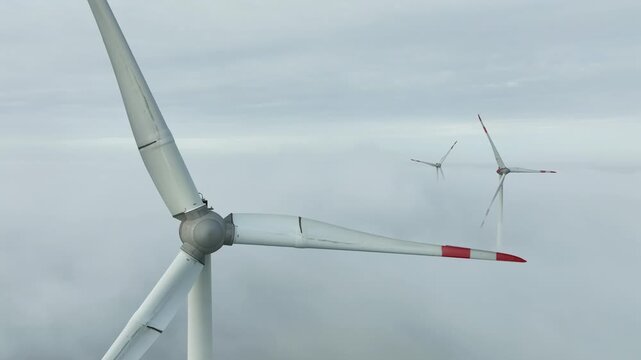 aerial footage of three wind turbines above the mist