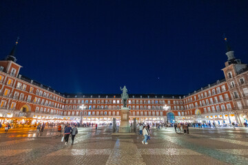 The bronze equestrian statue of King Philip III stands at the center of Madrid s Plaza Mayor at night. Soft golden lights illuminate the statue and the uniform, three-story residential buildings and