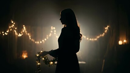Woman holding flower garland in dim light setting with glowing lights in background. Soft light illuminates room space. Concept of events, decoration, festivities