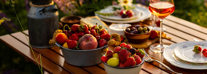 Banner. Beautiful elegant romantic dinner table decor, surprise day arrangement. Marriage proposal, engagement private party for two in a meadow. Sunset, golden hour. Cheese board, rose wine, fruits