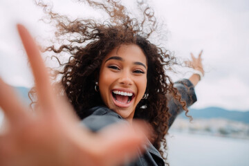 Smiling woman enjoying a joyful moment outdoors with wind in her hair against a scenic backdrop