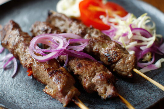 Savory lyulya kebab served with fresh vegetables and garnishes on a black plate during a meal setting