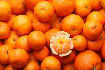Many whole tangerines and one peeled as background, top view