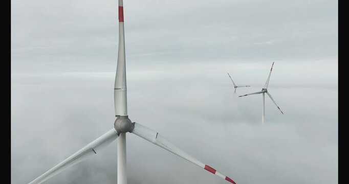 aerial footage of three wind turbines above the mist