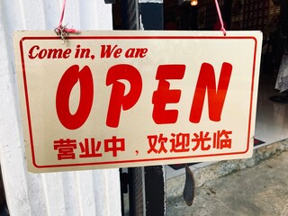 come in we are open sign in english and chinese hanging on the shop door