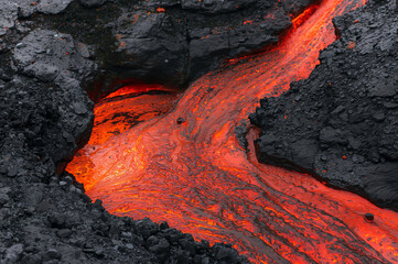Stream of glowing lava carving dark volcanic terrain