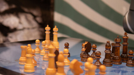 wooden chess pieces on board midgame, sunlit market stall setting with striped awning, shallow depth of field, warm tones, blue table surface, handcrafted pieces with patina, closeup focus