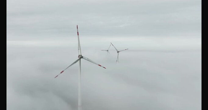 aerial footage of three wind turbines above the mist