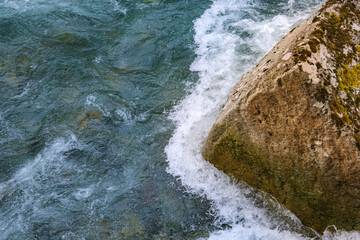 The powerful river flows rapidly. Creating whitewater foam as the water movement crashes against solid Immovable rock obstacle. Displaying a constant natural force. Perfect for resilience concepts.