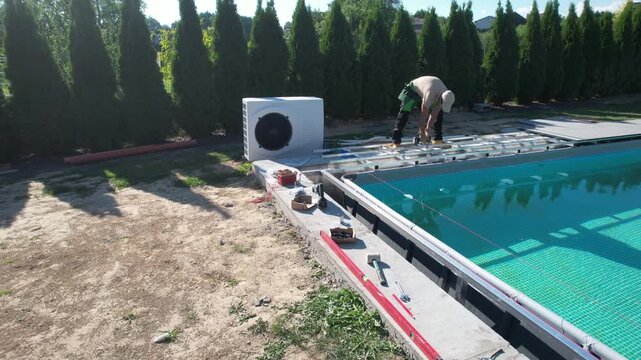 Worker Installs Equipment Next to a Swimming Pool in a Sunny Location