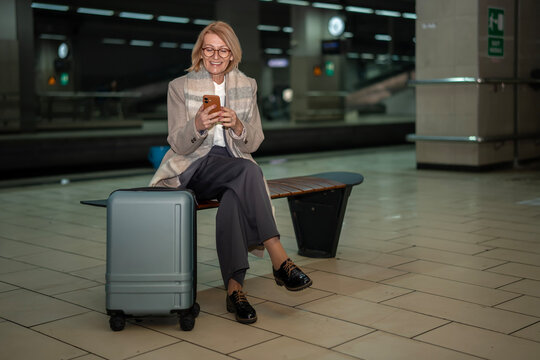 Mature woman smiling using smartphone at subway station
