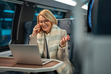 Mature woman traveling on train using laptop and phone