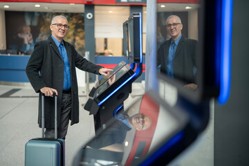 Senior man using airport self check-in kiosk