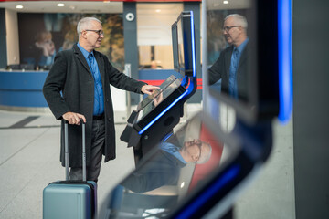 Senior man using self-service check-in kiosk at airport