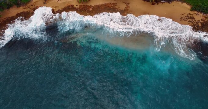 White-capped mighty waves splash on the narrow line of the sandy beach. Rising over the blue waterscape with raging waves.