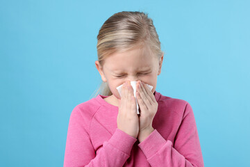 Little girl with runny nose on light blue background. Cold symptom