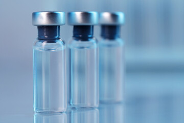Vaccine in glass vials on mirror surface against blurred grey background, closeup. Space for text
