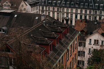 A panoramic cityscape of Zurich featuring historic church towers and rooftops under a cloudy sky. The image captures the charm of Switzerland old town with mountains in the background.