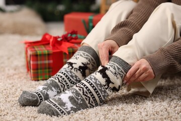 Woman putting on cozy socks and Christmas gifts on floor at home, closeup
