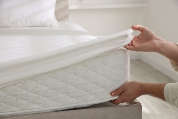 Man putting bed sheet on mattress indoors, closeup