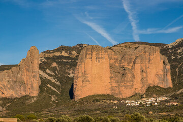 Fototapeta premium Olive Grove with the Mallos de Riglos Rock Formations and the Village of Riglos on a Sunny Day, Spain