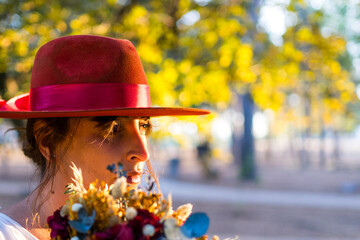 Profile portrait of a woman wearing a red hat and holding a bridal bouquet © Carbonero Stock
