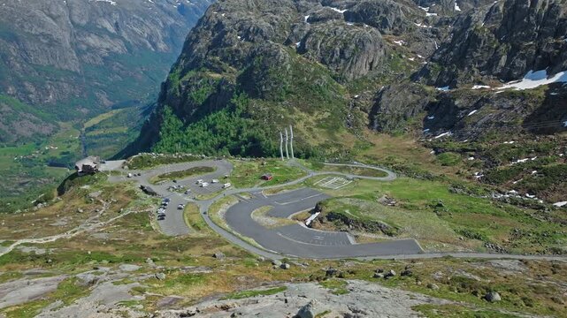 Aerial view of the Lysebotn hairpin road near Kjerag in Norway. Drone footage shows dramatic mountain switchbacks, green valley and rugged cliffs on a clear summer day.