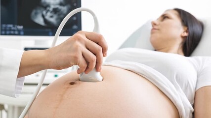 Doctor performing prenatal ultrasound scan on pregnant woman's belly during medical checkup. Scanning pregnant woman's belly to monitor fetal development and maternal health.
