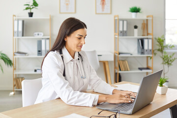 Female doctor or nurse is working with a laptop in a hospital office. The medical professional is...