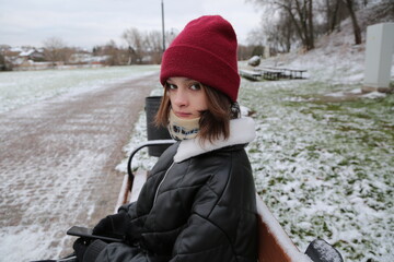 Young woman sitting on the bench in winter snow city park background
