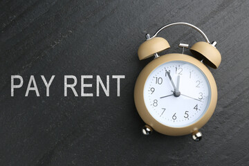 Time to pay rent. Alarm clock on dark grey stone background, top view