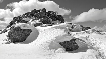 Wind-blown snow forming subtle drifts against rugged rocky mountain peaks under a cloudy winter sky.