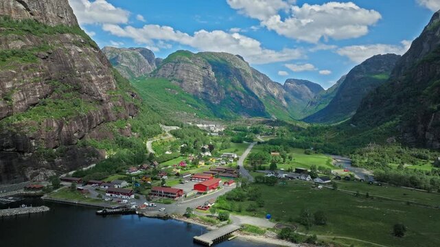 Aerial panorama of Lysebotn village beside Lysefjord, Norway. The drone reveals red rooftops, harbor area and towering cliffs under clear skies in summertime.