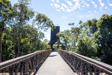 Upper view of Bosque Alemão in Curitiba, Paraná, Brazil. The scene features a German-inspired wooden building with traditional architectural elements, a cascading water feature in the foreground, and 