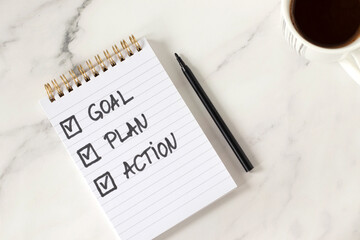 Goal, plan, action, handwritten inspirational checklist text in notebook with coffee cup on white marble background. New year resolutions, personal growth, business progress and success concept.