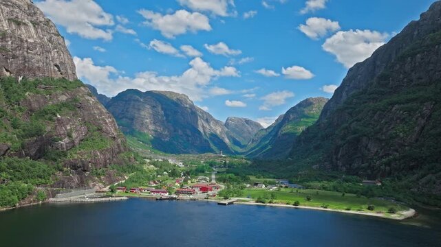 Wide aerial panorama of Lysefjord and Lysebotn village in Norway. The drone captures dramatic cliffs, calm water and a quiet fjord community on a clear day.