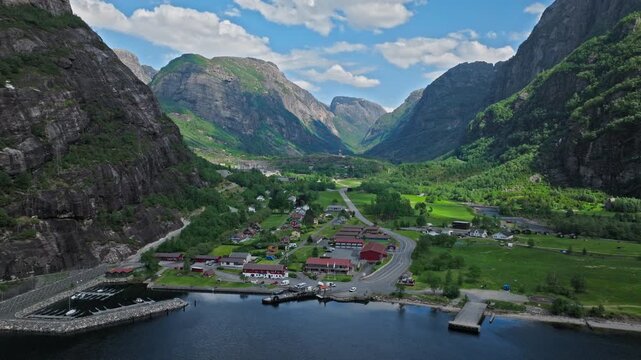 High altitude drone footage of Lysebotn village in Lysefjord, Norway. Scenic overview shows roads, houses and harbor nestled between dramatic cliffs.