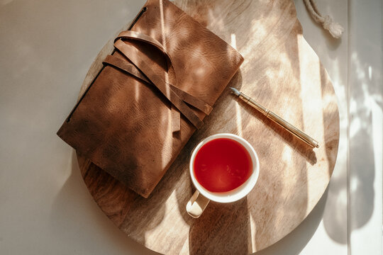 notebook sitting on a wooden board with pen and cup of tea on the side