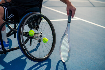 A male wheelchair tennis player is ready, holding a racquet near tennis balls on the court.