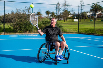 A man in a wheelchair focuses on hitting a tennis ball during practice
