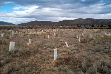 A wide angle view of the cemetery at the Stewart Indian School, showing grave markers and the surrounding Great Basin landscape under a cloudy sky.